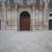 Il corpo centrale  costituito dal portale ad arco a tutto sesto che racchiude il massiccio portone in legno, il tutto inquadrato da colonne in stile ionico e da lesene binate che sostengono un balcone mistilineo in ferro
